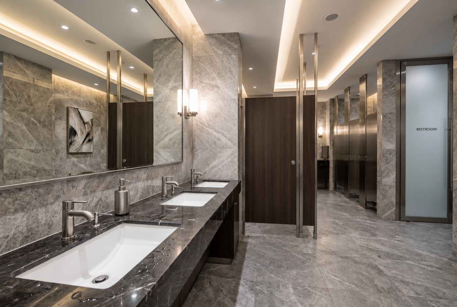 Professional commercial restroom cleaning service in a luxury office bathroom with marble countertops, modern fixtures, and premium finishes. Floor-cleaning equipment and sanitation tools highlight janitorial services, restroom disinfection, workplace hygiene, and commercial facility maintenance in a corporate environment.