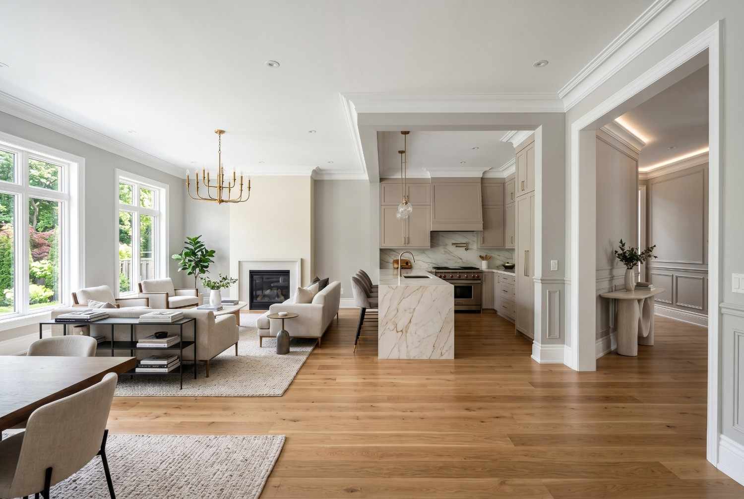 Elegant open-concept living room and kitchen with marble waterfall island, hardwood flooring, custom cabinetry, fireplace, and designer lighting. Luxury home interior featuring premium finishes, spacious layout, natural light, and sophisticated contemporary residential design.