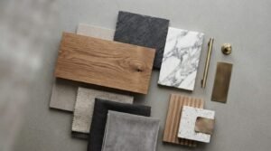 A curated flat lay material mood board on concrete featuring an oak wood plank, Calacatta marble slab, textured black slate, terrazzo tile, brushed brass hardware, and textile swatches