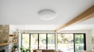 White circular wireless access point with an illuminated LED indicator ring mounted flush on a ceiling in a modern living room