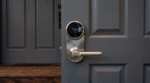 A brushed nickel smart electronic door lock with a digital touchscreen keypad and knurled handle installed on a modern dark gray paneled entryway door