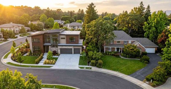 Modern and traditional homes side by side in a tree-lined suburban neighborhood viewed from above at sunset.