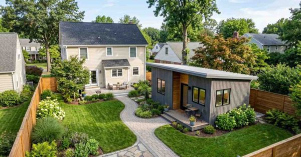 Modern backyard ADU with landscaped lawn, curved stone walkway, and main suburban home in the background.