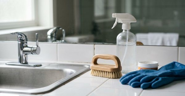 Cleaning supplies, gloves, and a scrub brush arranged beside a bathroom sink for mold removal and surface cleaning.