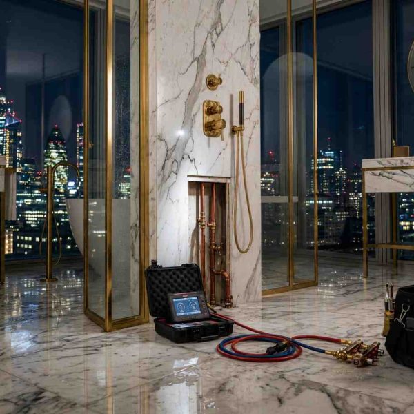 Professional plumber repairing a leaking bathroom pipe in a luxury high-rise apartment, using advanced leak detection equipment and plumbing tools. Emergency plumbing service addressing water damage and pipe repair in a modern marble bathroom, with city skyline views and residential maintenance expertise.