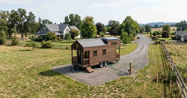 Tiny house on wheels positioned on a residential property with visible trailer chassis, driveway access, property boundaries, setbacks, utilities, survey markers, and surrounding structures.